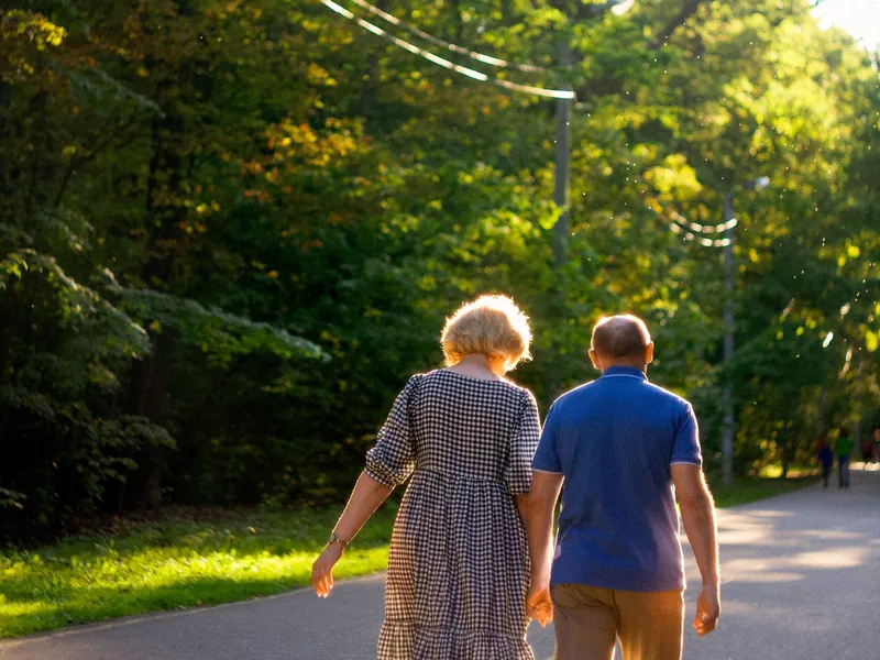 An older couple walking together along a tree-lined path in the morning.
