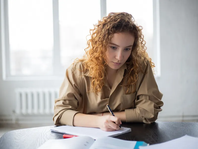 A young woman writing notes at a desk in daylight.
